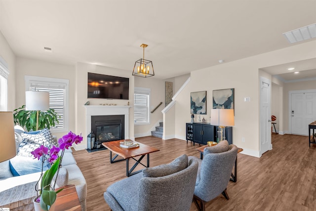 living room featuring a glass covered fireplace, stairs, baseboards, wood finished floors, and visible vents