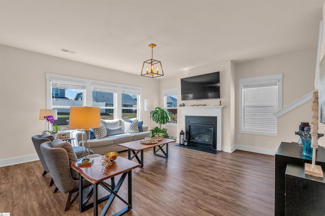 living area featuring baseboards, a glass covered fireplace, wood finished floors, and an inviting chandelier