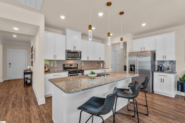 kitchen featuring a kitchen island with sink, backsplash, appliances with stainless steel finishes, a sink, and white cabinets