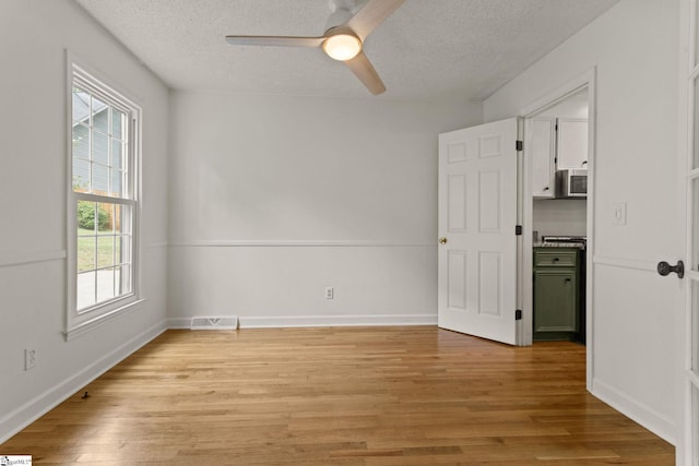 empty room with a ceiling fan, a textured ceiling, visible vents, and light wood-style flooring