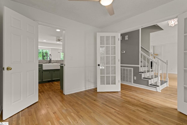 spare room with visible vents, ceiling fan, french doors, a sink, and light wood-style flooring