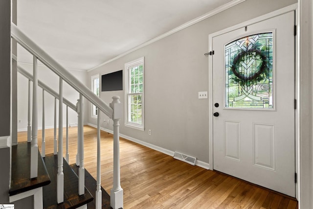 foyer entrance with visible vents, crown molding, baseboards, light wood-style floors, and stairs