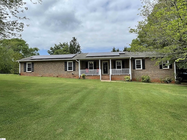 single story home featuring a porch, brick siding, roof mounted solar panels, and a front lawn