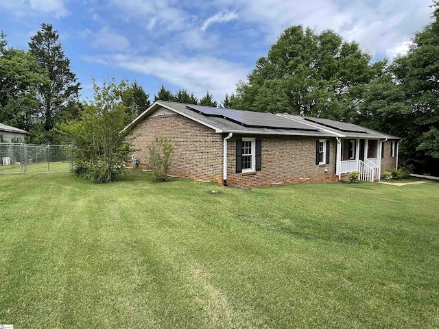 view of side of property featuring a porch, brick siding, fence, roof mounted solar panels, and a yard
