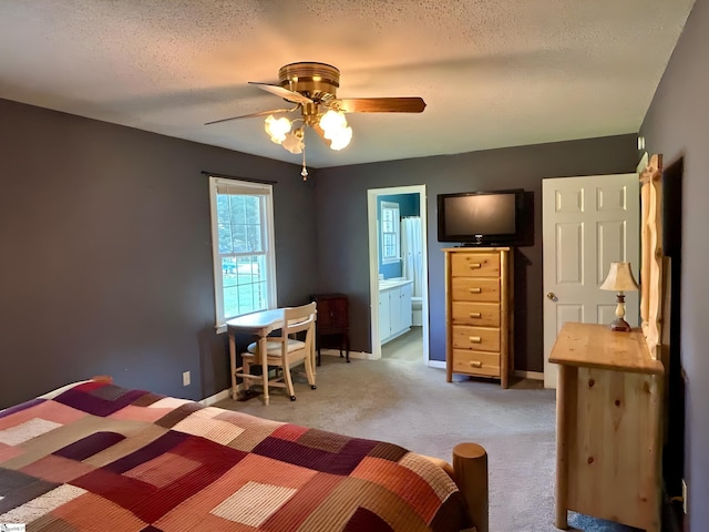 bedroom featuring ceiling fan, light carpet, a textured ceiling, baseboards, and ensuite bathroom
