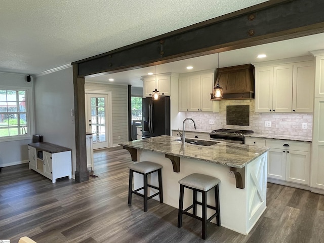 kitchen featuring stainless steel gas range oven, a sink, dark wood finished floors, premium range hood, and black fridge with ice dispenser