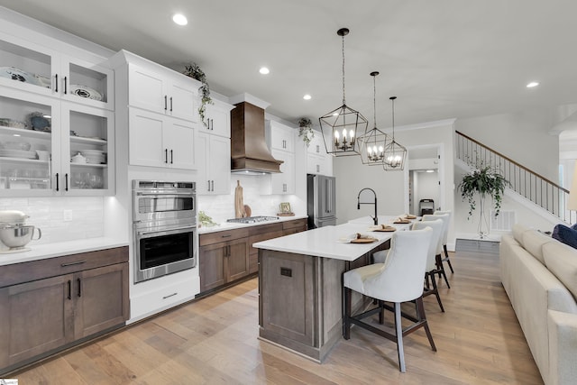 kitchen featuring decorative backsplash, a breakfast bar, light countertops, wall chimney exhaust hood, and stainless steel appliances