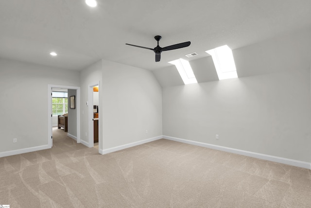 spare room featuring vaulted ceiling with skylight, a ceiling fan, baseboards, light carpet, and recessed lighting