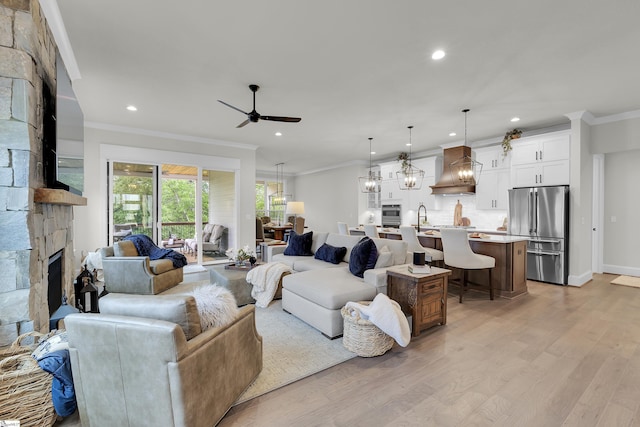 living room featuring ceiling fan, light wood-style floors, a stone fireplace, recessed lighting, and ornamental molding