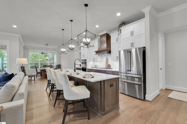 kitchen featuring light countertops, premium range hood, ornamental molding, stainless steel appliances, and an island with sink