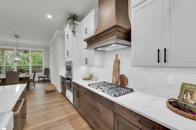 kitchen with light countertops, stainless steel appliances, ornamental molding, and custom range hood