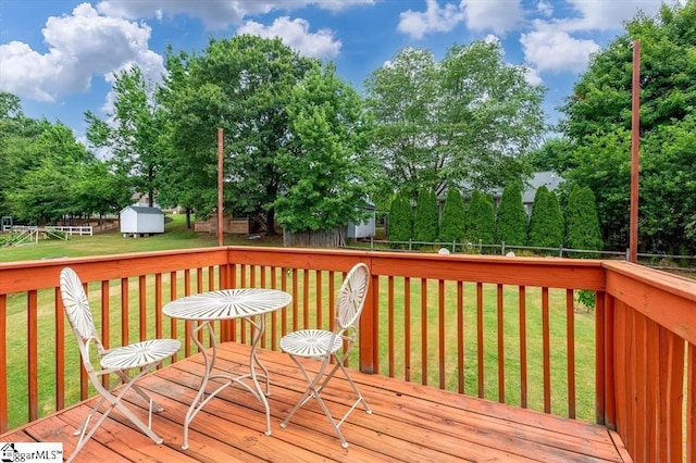 wooden terrace with a storage unit, an outdoor structure, a lawn, and a fenced backyard