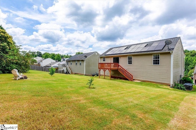 back of house featuring solar panels, a deck, stairway, fence, and a yard