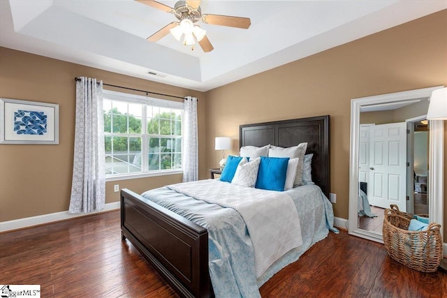 bedroom featuring ceiling fan, visible vents, a raised ceiling, baseboards, and dark wood-style floors