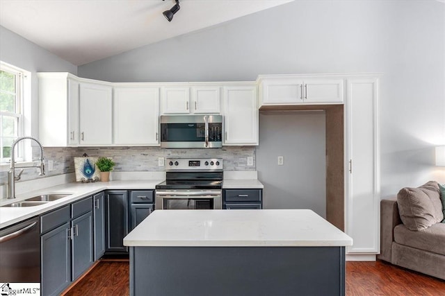 kitchen featuring backsplash, appliances with stainless steel finishes, vaulted ceiling, a sink, and white cabinetry