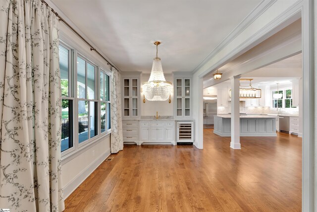 unfurnished dining area with beverage cooler, light wood finished floors, crown molding, and an inviting chandelier