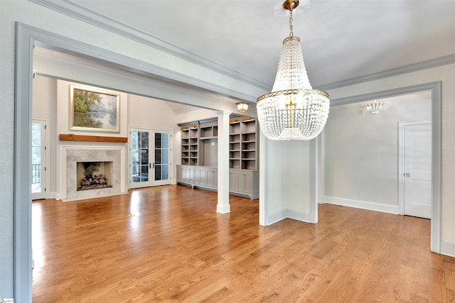 unfurnished dining area featuring crown molding, a fireplace, baseboards, light wood finished floors, and a notable chandelier