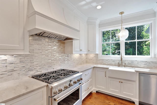 kitchen with decorative light fixtures, crown molding, custom range hood, stainless steel appliances, and white cabinetry