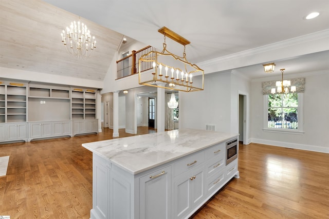 kitchen with a kitchen island, baseboards, light wood-type flooring, stainless steel microwave, and a chandelier