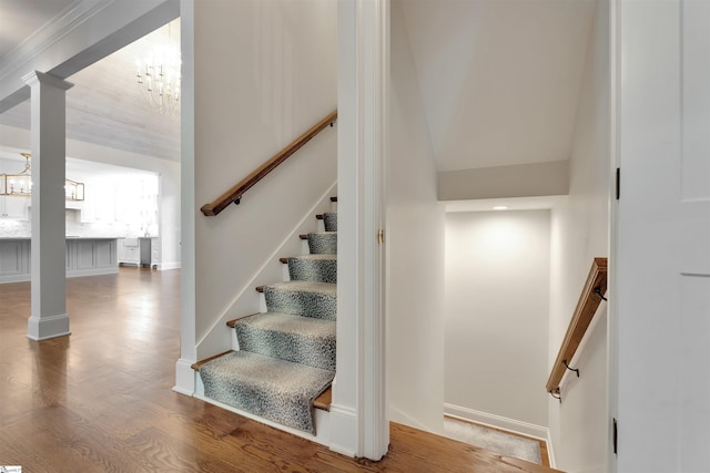 stairway featuring an inviting chandelier, decorative columns, and wood finished floors