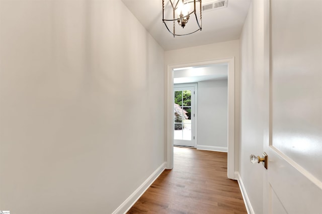 corridor featuring baseboards, a notable chandelier, visible vents, and wood finished floors