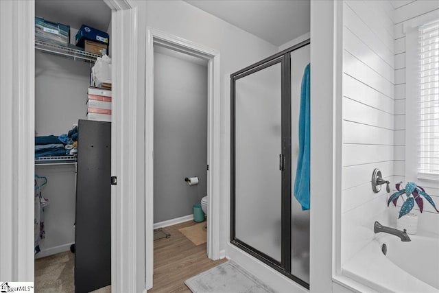 full bath featuring a walk in closet, a shower stall, toilet, and wood finished floors
