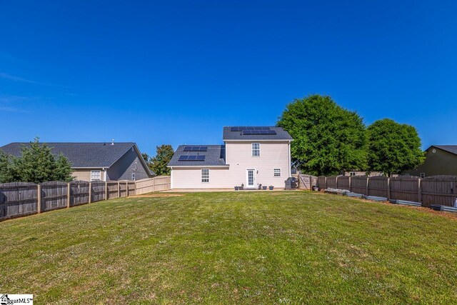 back of property with a fenced backyard, a patio, a yard, and solar panels