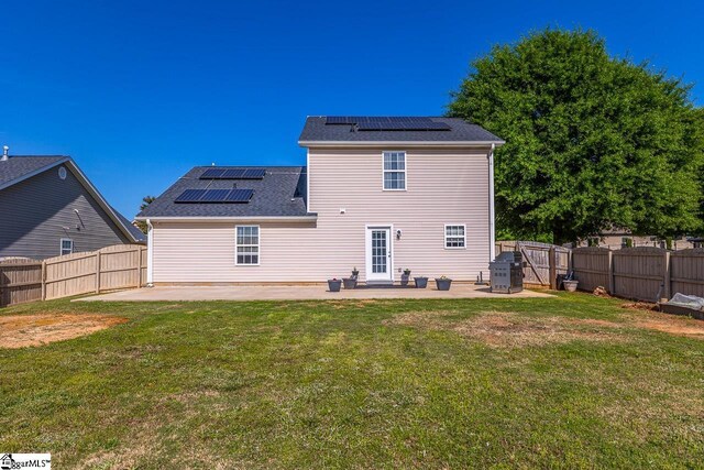 rear view of property with a fenced backyard, solar panels, a yard, and a patio area