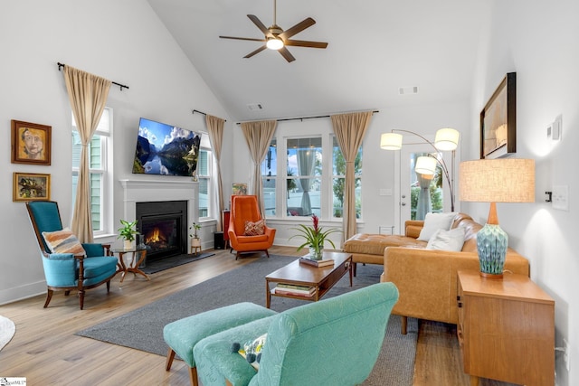 living area featuring visible vents, wood finished floors, a lit fireplace, high vaulted ceiling, and a ceiling fan
