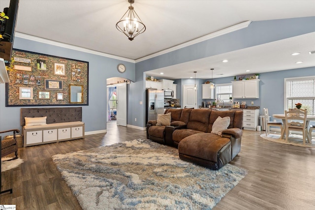 living area with a healthy amount of sunlight, ornamental molding, wood finished floors, and a notable chandelier