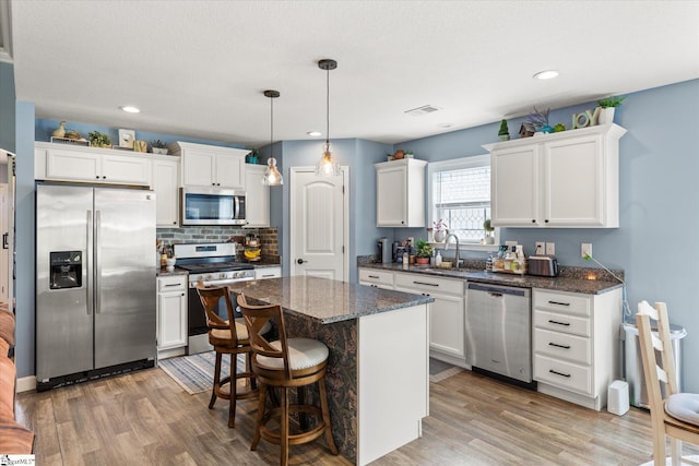 kitchen with a sink, light wood-style floors, stainless steel appliances, white cabinetry, and a kitchen island