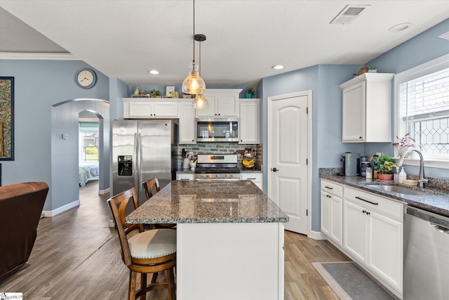 kitchen featuring a sink, white cabinets, arched walkways, light wood finished floors, and appliances with stainless steel finishes