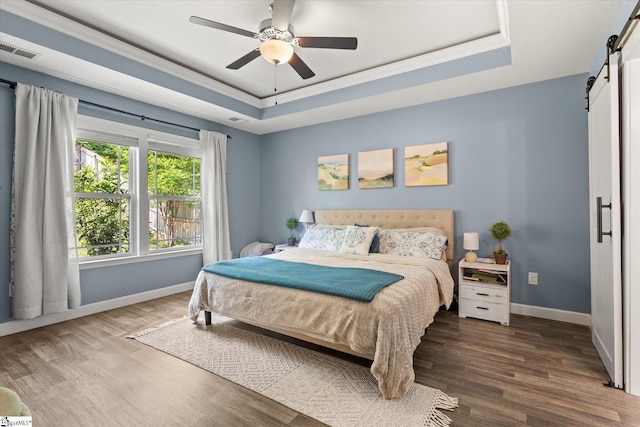 bedroom featuring a barn door, baseboards, wood finished floors, a tray ceiling, and visible vents