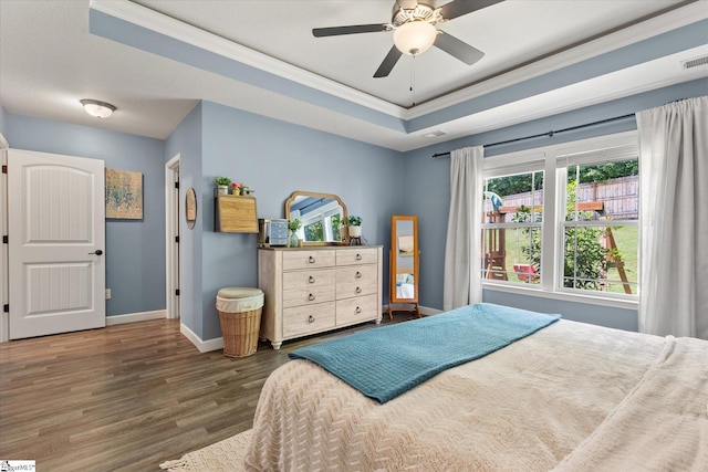 bedroom with visible vents, crown molding, wood finished floors, baseboards, and a tray ceiling