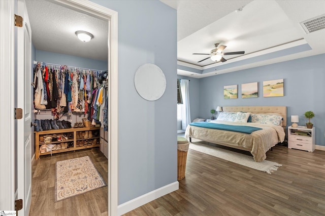bedroom featuring visible vents, wood finished floors, baseboards, ceiling fan, and a tray ceiling
