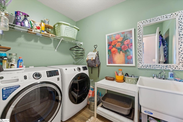laundry room featuring laundry area, wood finished floors, a textured ceiling, washing machine and clothes dryer, and a sink