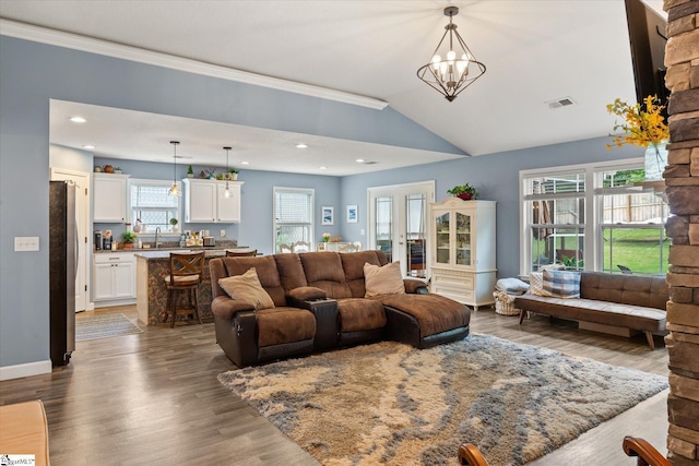 living room with an inviting chandelier, wood finished floors, vaulted ceiling, visible vents, and ornamental molding