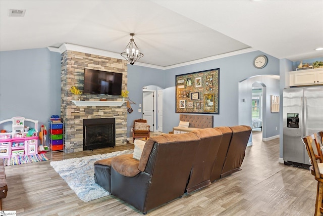 living room with an inviting chandelier, arched walkways, light wood finished floors, and a fireplace