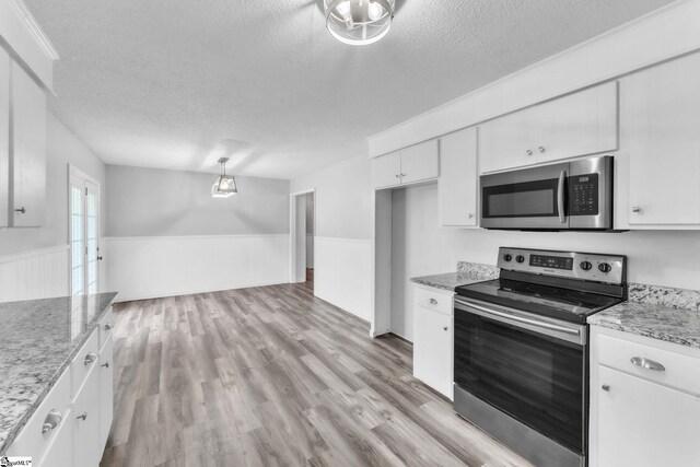 kitchen featuring wainscoting, a textured ceiling, white cabinetry, light wood-style flooring, and stainless steel appliances