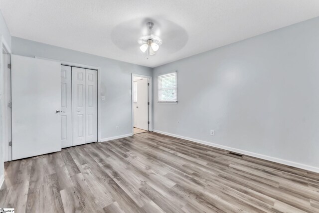 unfurnished bedroom featuring ceiling fan, visible vents, wood finished floors, baseboards, and a closet