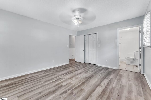 unfurnished bedroom with a closet, wood finished floors, baseboards, ceiling fan, and connected bathroom