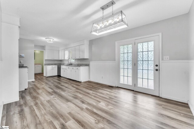 kitchen featuring a wainscoted wall, white cabinets, a sink, light wood finished floors, and dishwasher