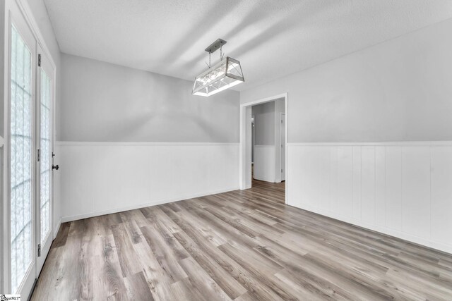 unfurnished dining area with a textured ceiling, wainscoting, and wood finished floors