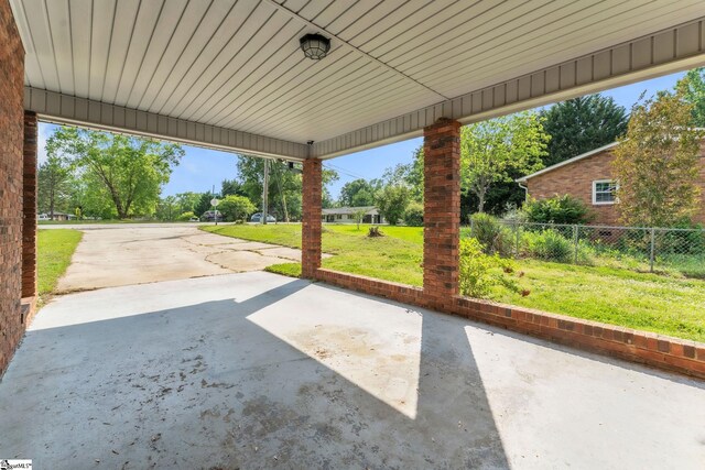 view of patio / terrace with concrete driveway, fence, and a carport
