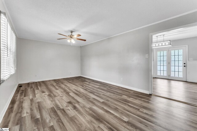 empty room with a textured ceiling, a ceiling fan, baseboards, wood finished floors, and ornamental molding