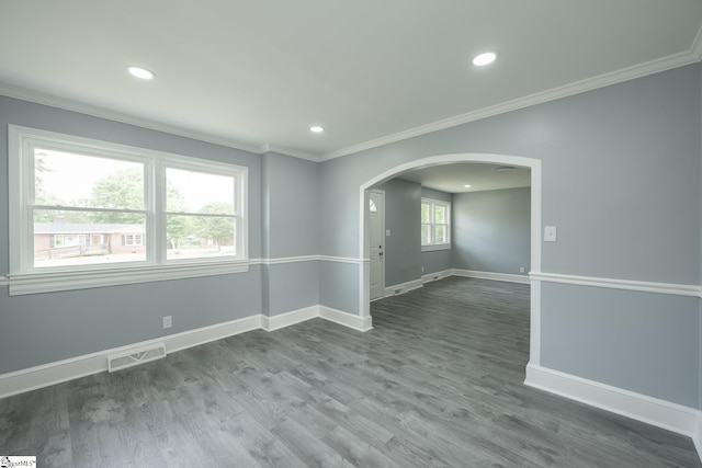 unfurnished room with arched walkways, baseboards, wood finished floors, visible vents, and ornamental molding