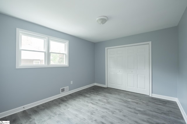 unfurnished bedroom with visible vents, baseboards, wood finished floors, and a closet