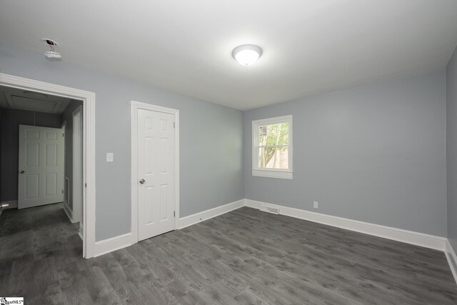 unfurnished bedroom featuring baseboards, attic access, and dark wood finished floors