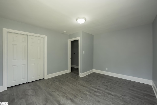 unfurnished bedroom featuring baseboards, dark wood-style floors, and a closet