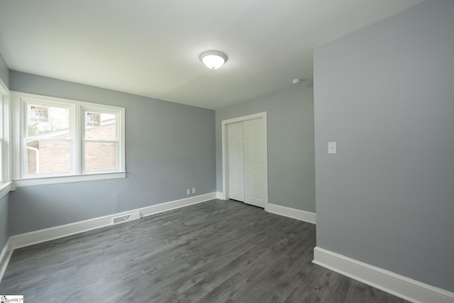 unfurnished bedroom with baseboards, visible vents, dark wood-style floors, and a closet